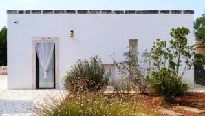 Un edificio blanco con una ventana pequeña y una puerta, rodeado de plantas y flores.
