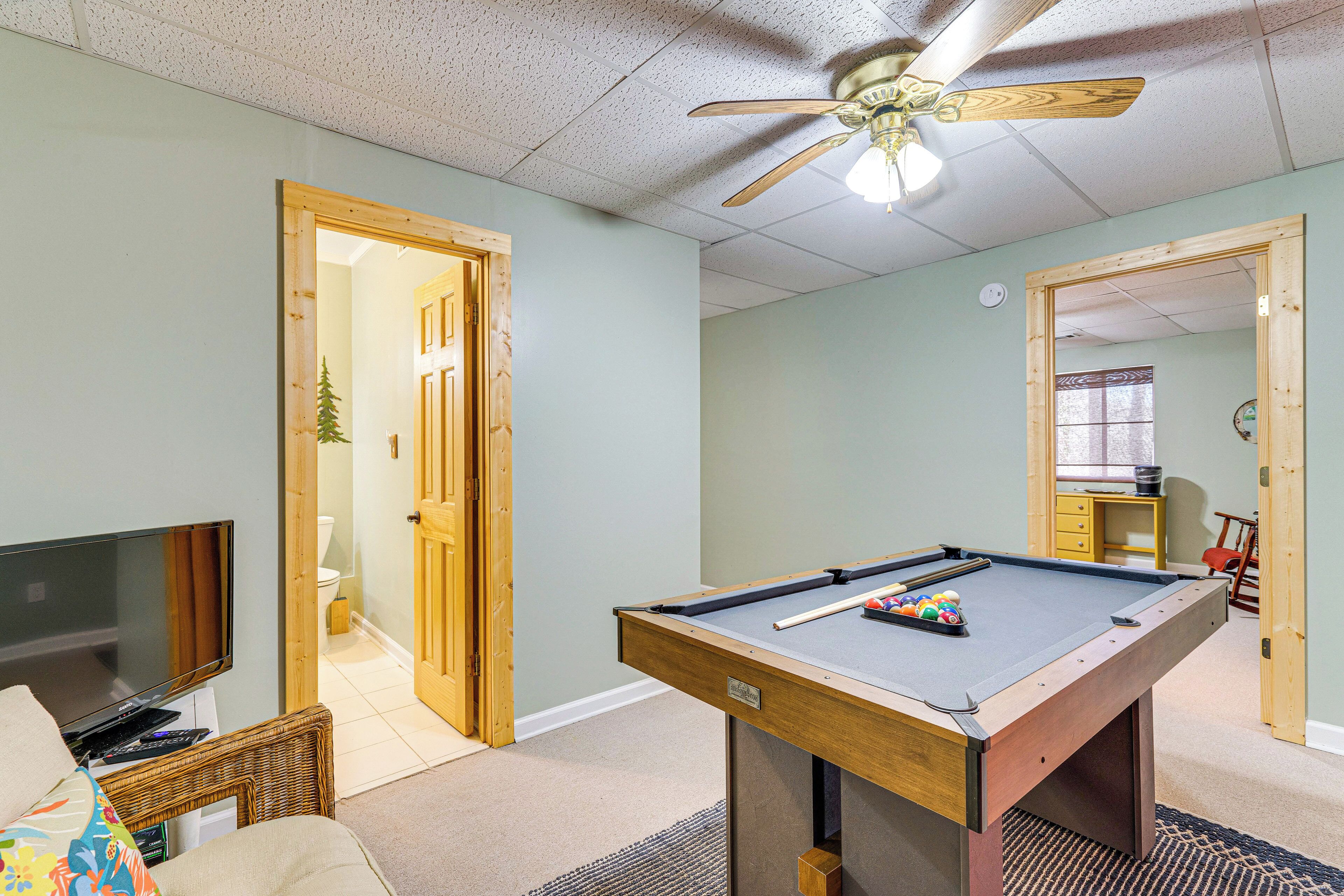 A room with a pool table, a television, and a ceiling fan.