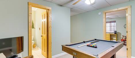 A room with a pool table, a television, and a ceiling fan.