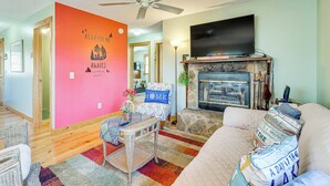 A living room with a fireplace, a ceiling fan, a television, and a colorful wall. - Pet-friendly Hiawassee Cabin w/ Lake Views & Sauna (Hiawassee)