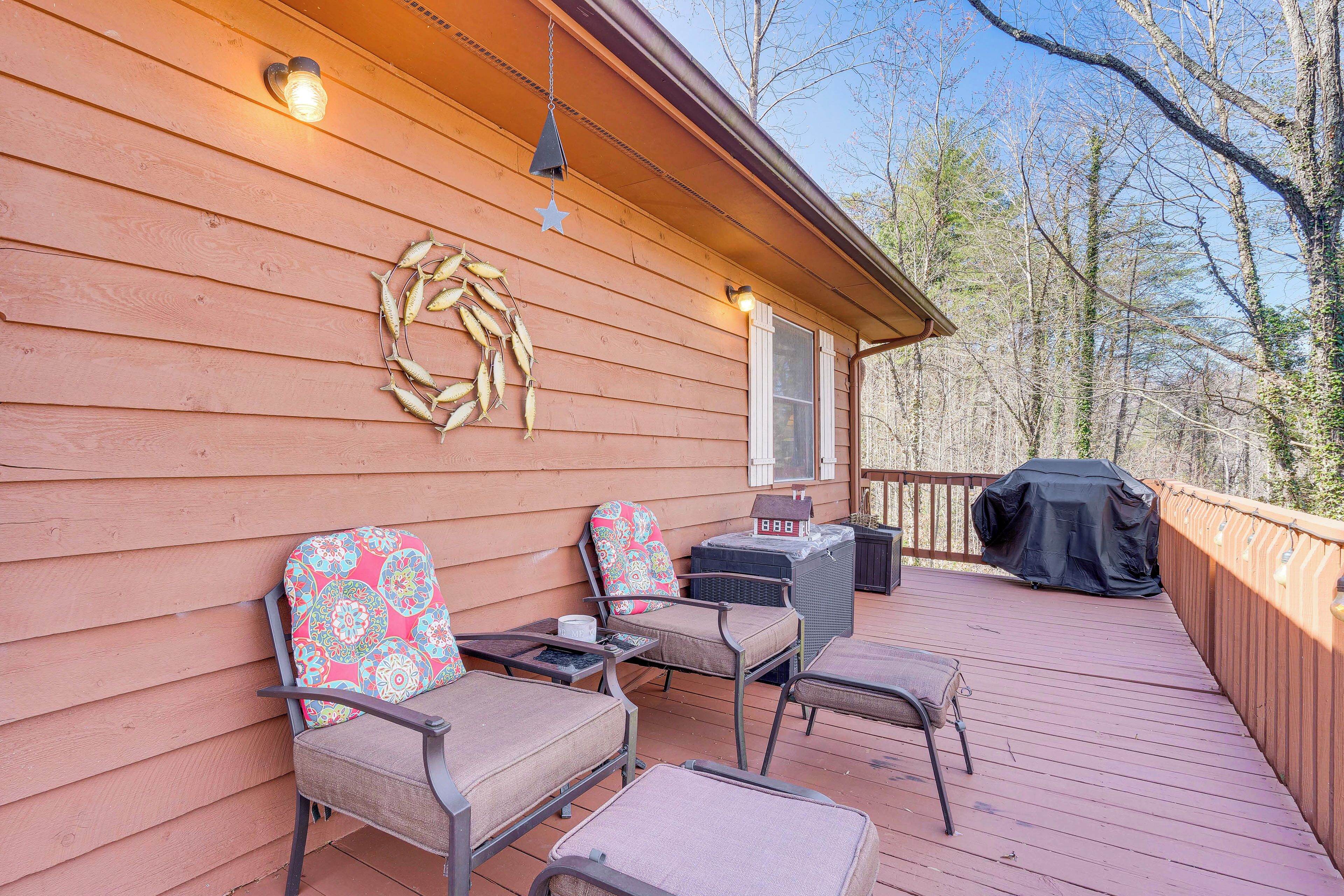 Une terrasse en bois avec des meubles d’extérieur, un barbecue couvert et une guirlande décorative accrochée au mur.