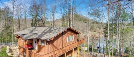 A wooden cabin with a balcony, surrounded by trees and a hillside.