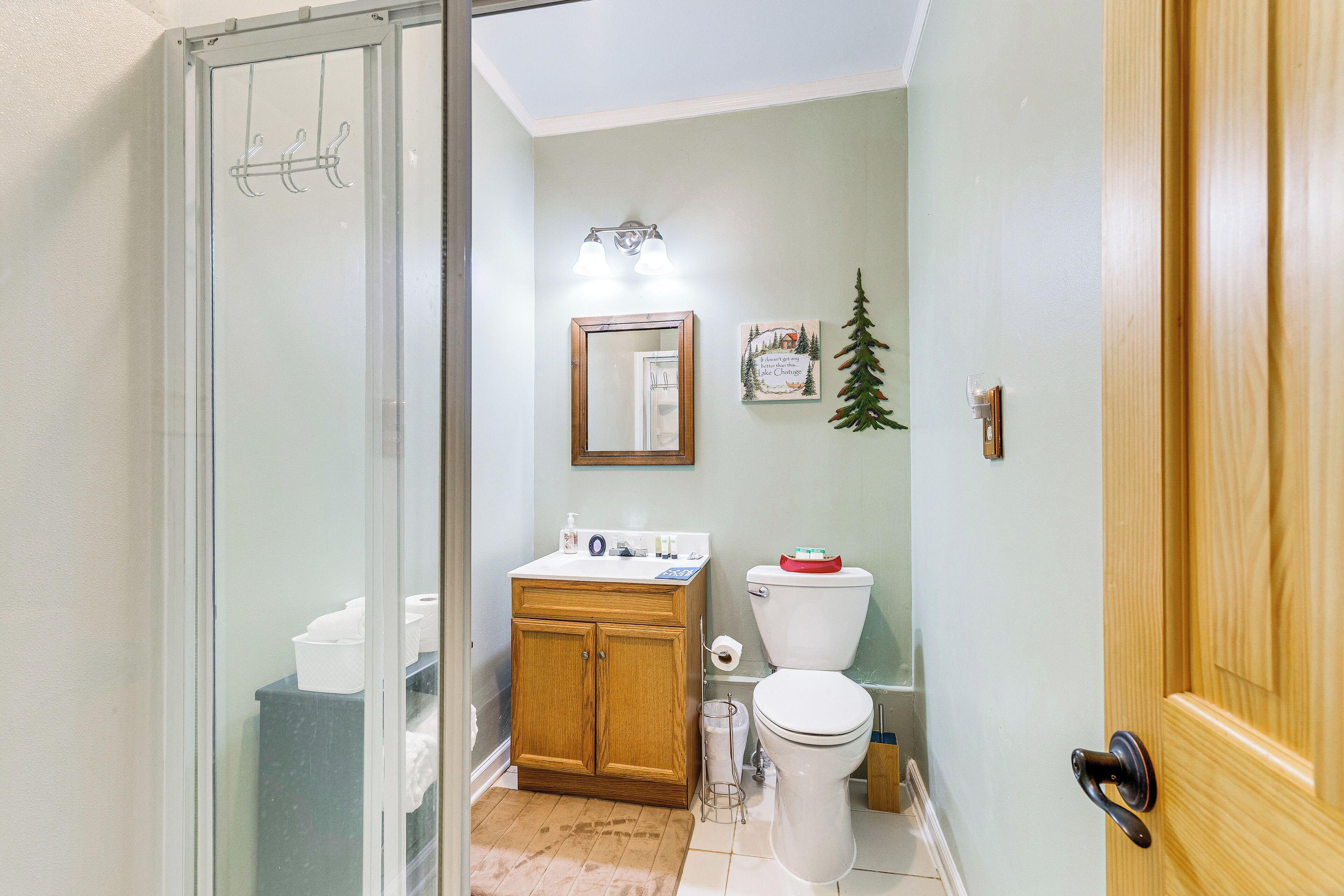 A bathroom with a glass shower enclosure, wooden cabinets, a white toilet, and a sink with a soap dispenser.