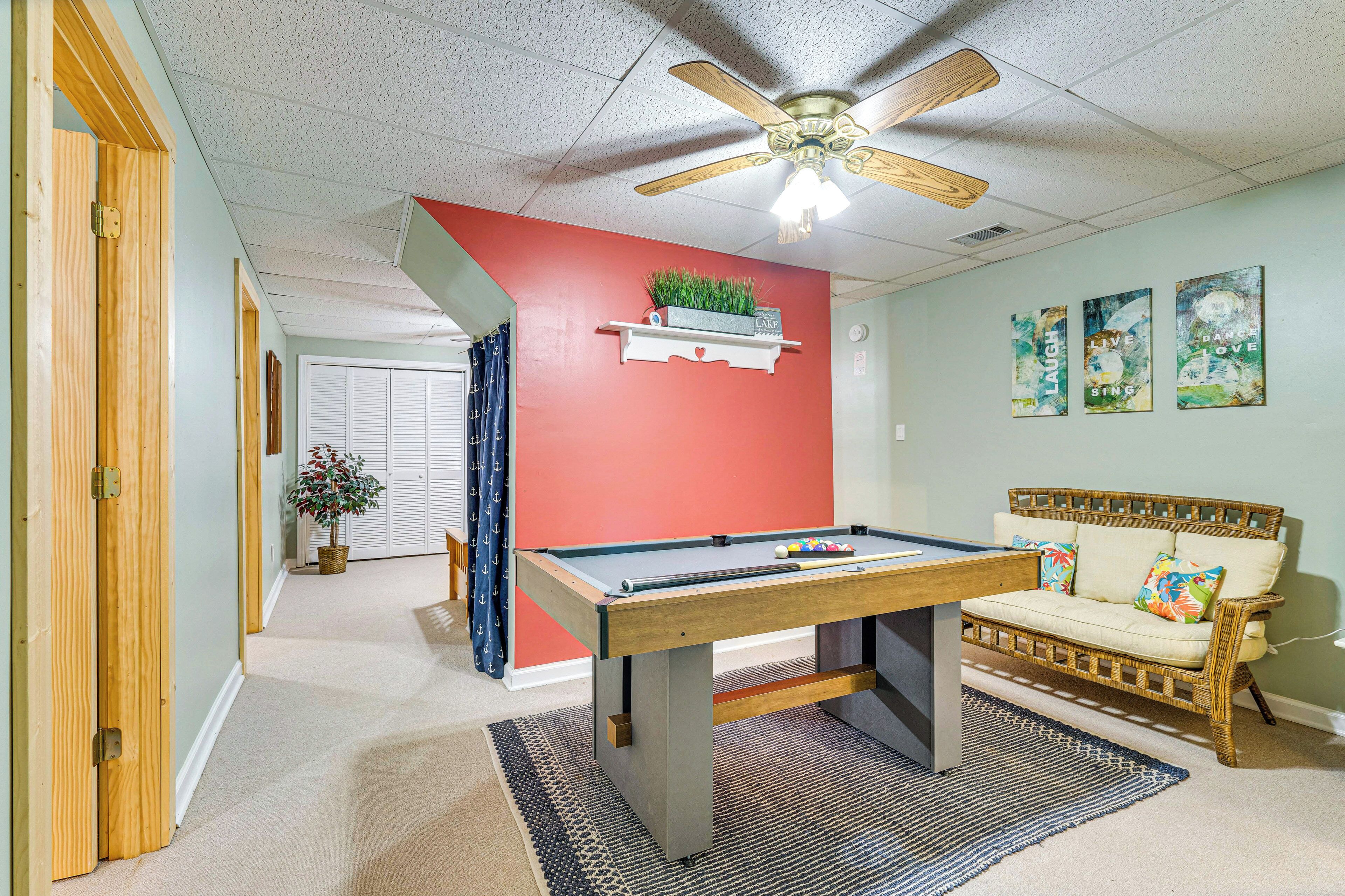 A room with a pool table, a ceiling fan, a sofa, and a wall-mounted shelf with a plant.