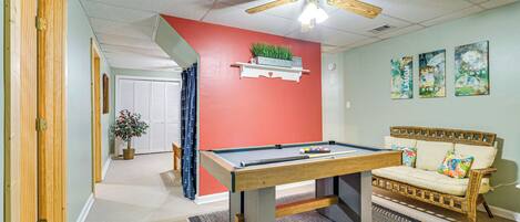 A room with a pool table, a ceiling fan, a sofa, and a wall-mounted shelf with a plant.