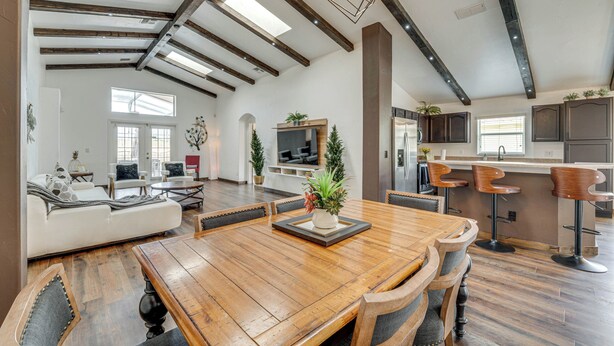 A spacious living area with a wooden dining table, comfortable seating, a kitchen area, and a high ceiling with exposed beams.