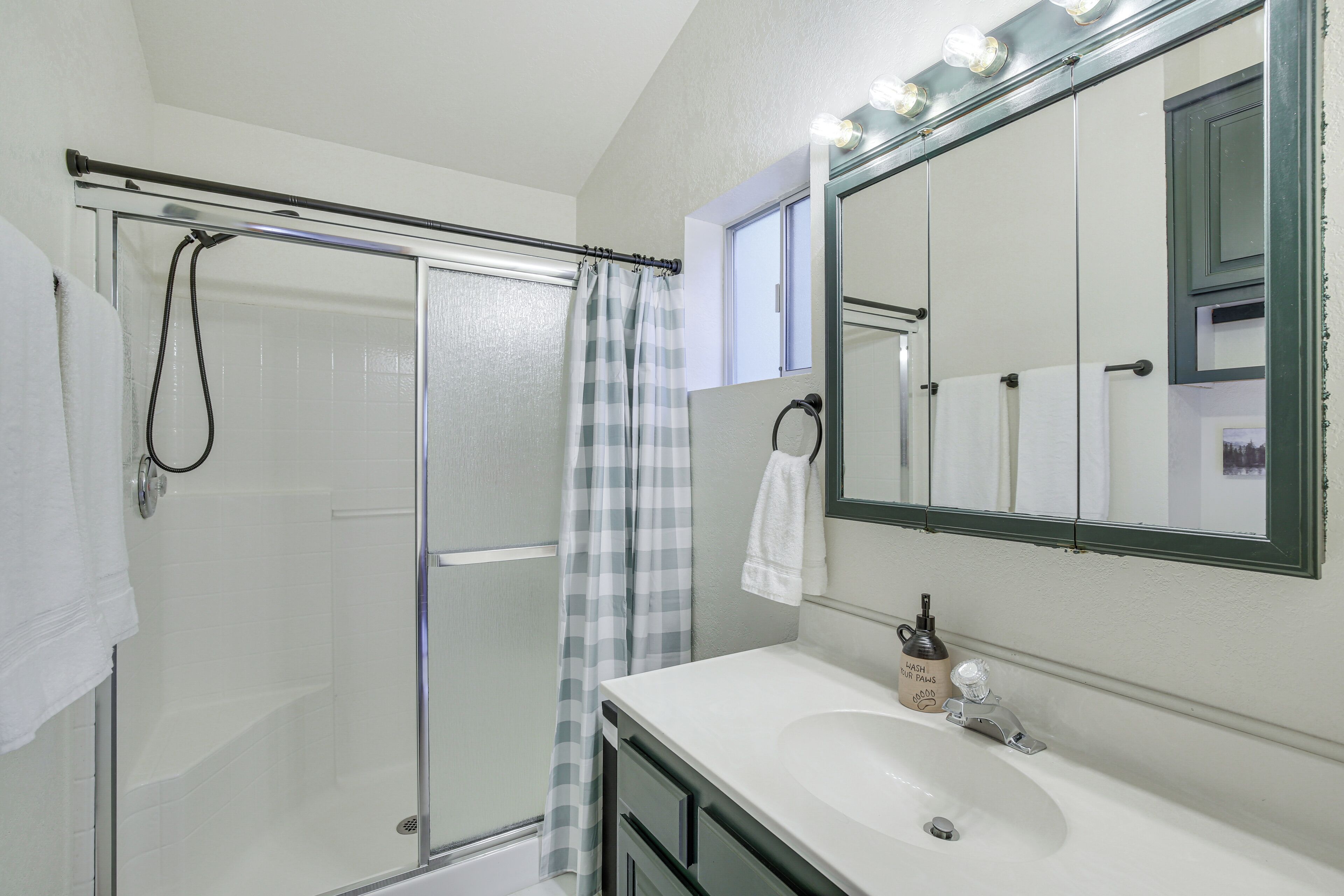 A bathroom with a glass shower enclosure, a white sink, and a large mirror with lights above it.