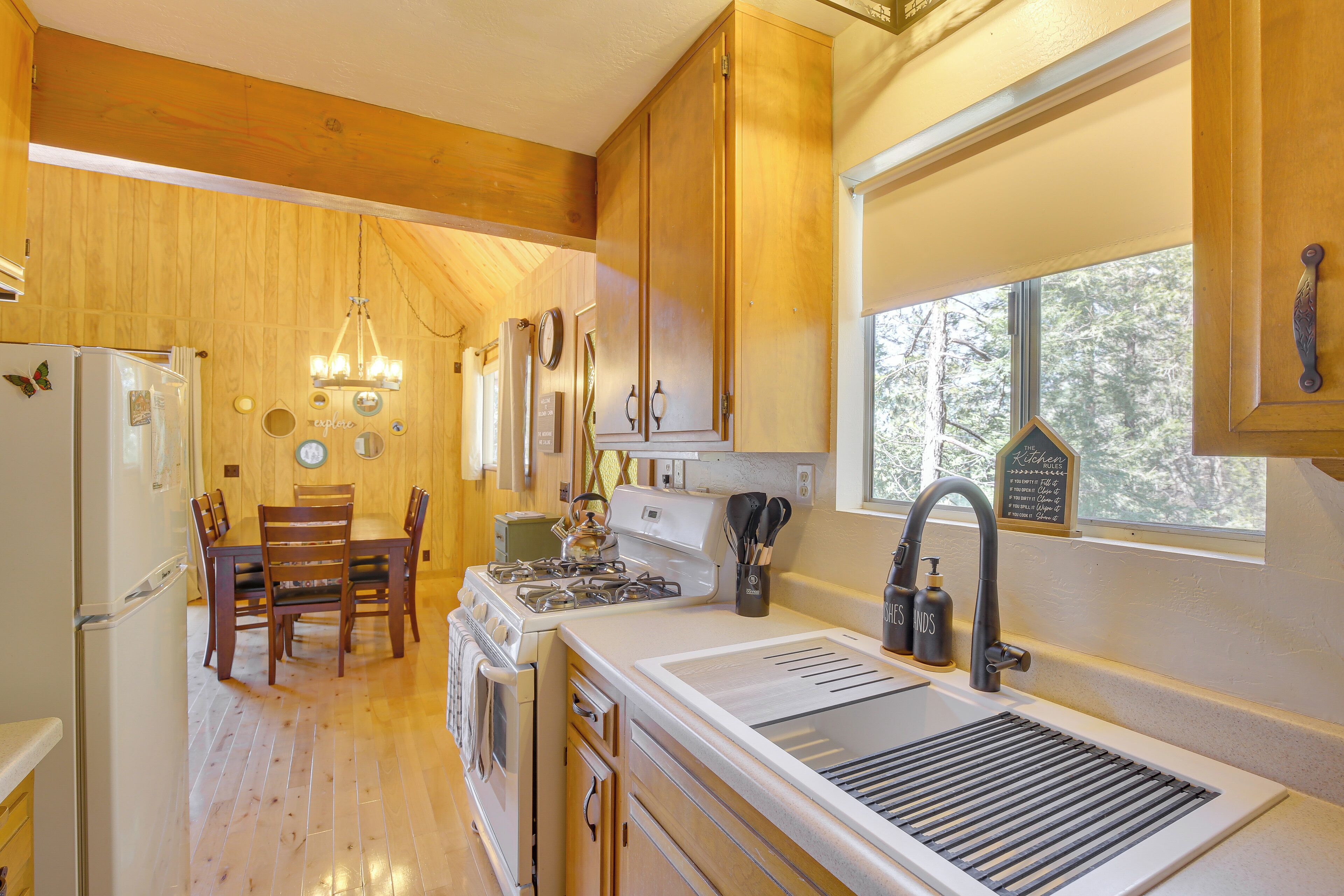 A kitchen with wooden cabinets, a stove, a sink, and a dining area with chairs.