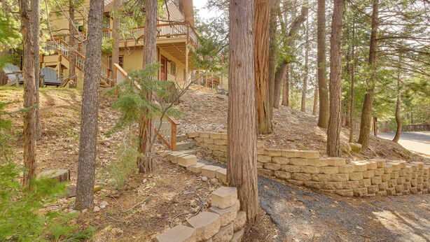 A two-story building with a stone staircase leading up to a wooden deck, surrounded by trees.
