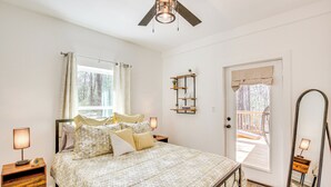 A bedroom with a bed, bedside tables, a ceiling fan, a window with curtains, a door leading to an outdoor deck, and a wall-mounted shelf with plants. - Winnsboro Barndominium w/ Fire Pit & Large Deck! (Winnsboro)