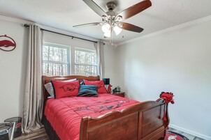 Un dormitorio con cama de madera, ventilador de techo, ventana con cortinas y un adorno en la pared.