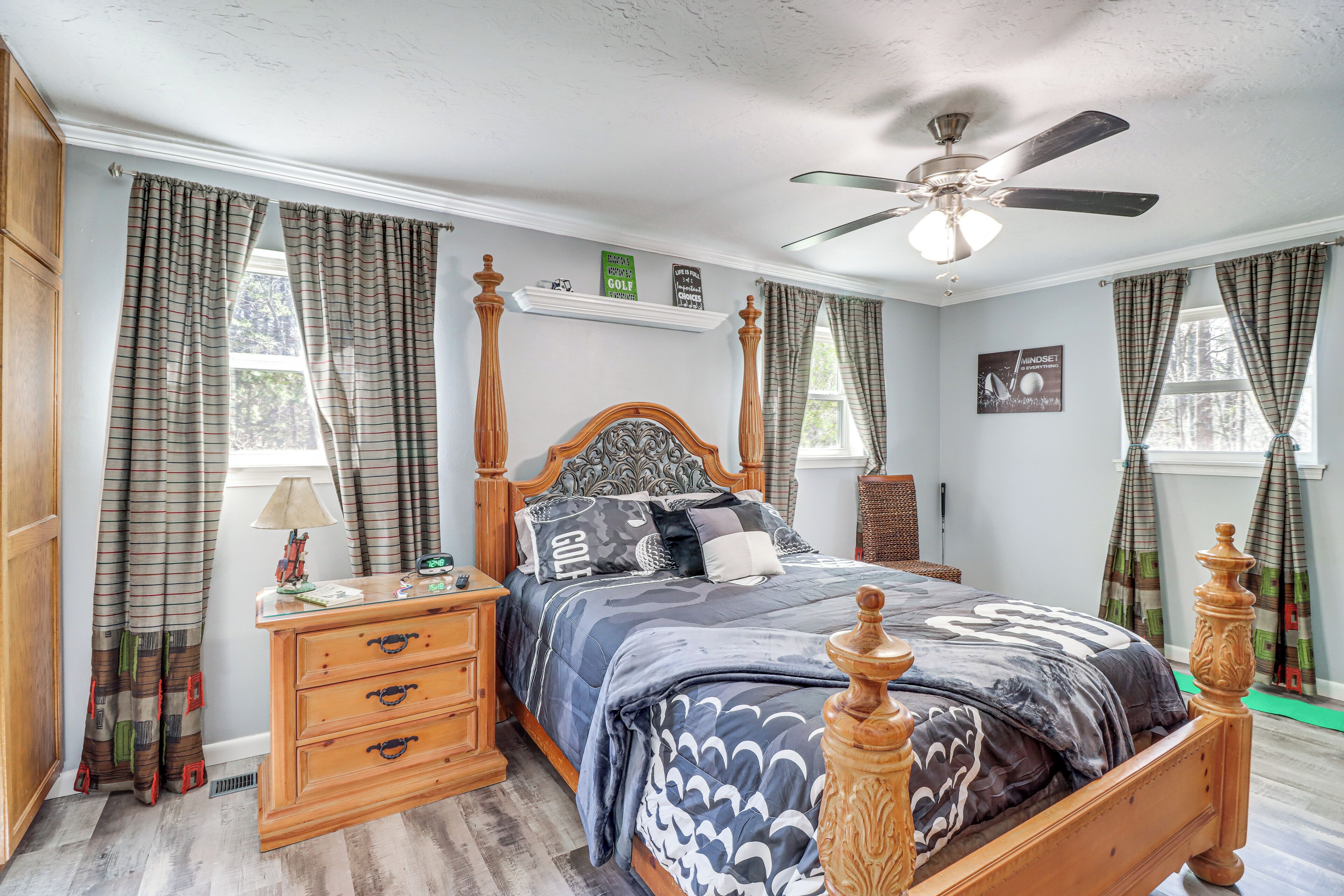 A bedroom with a wooden four-poster bed, a ceiling fan, and plaid curtains.