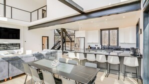 Une cuisine moderne dotée d’un îlot central, d’un coin repas avec une grande table et des chaises, et d’un escalier reliant les deux étages.