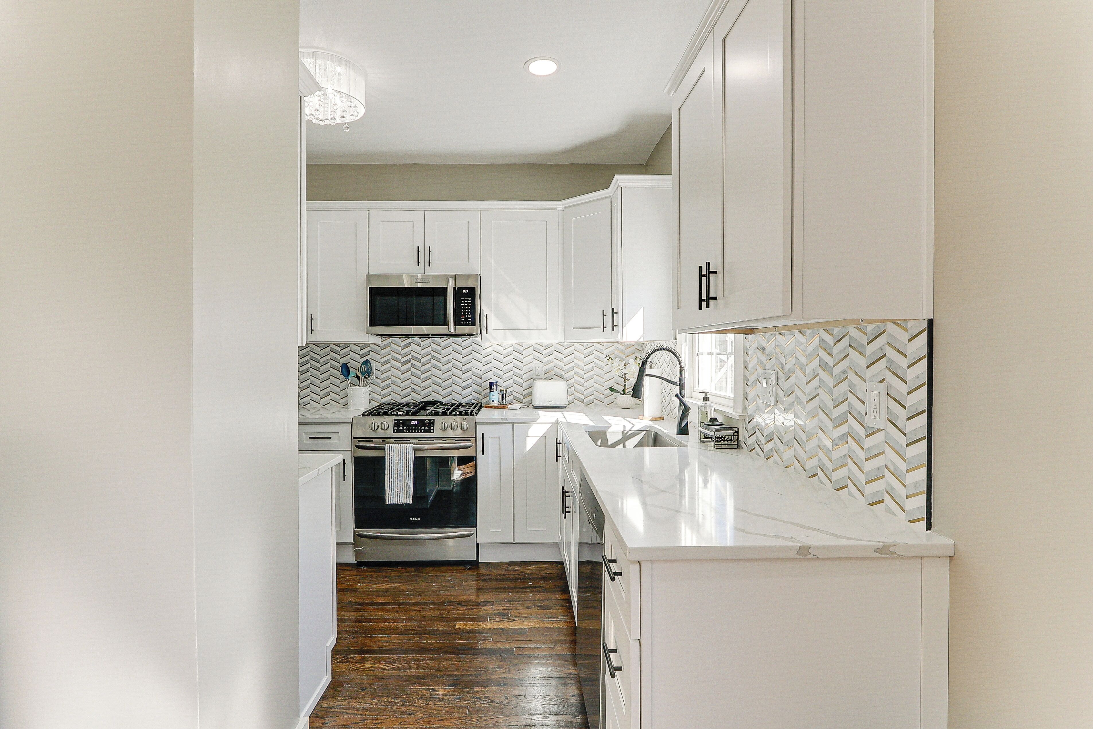 A modern kitchen with white cabinetry, a microwave, an oven, and a herringbone-patterned backsplash.
