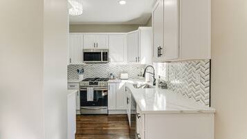 A modern kitchen with white cabinetry, a microwave, an oven, and a herringbone-patterned backsplash.