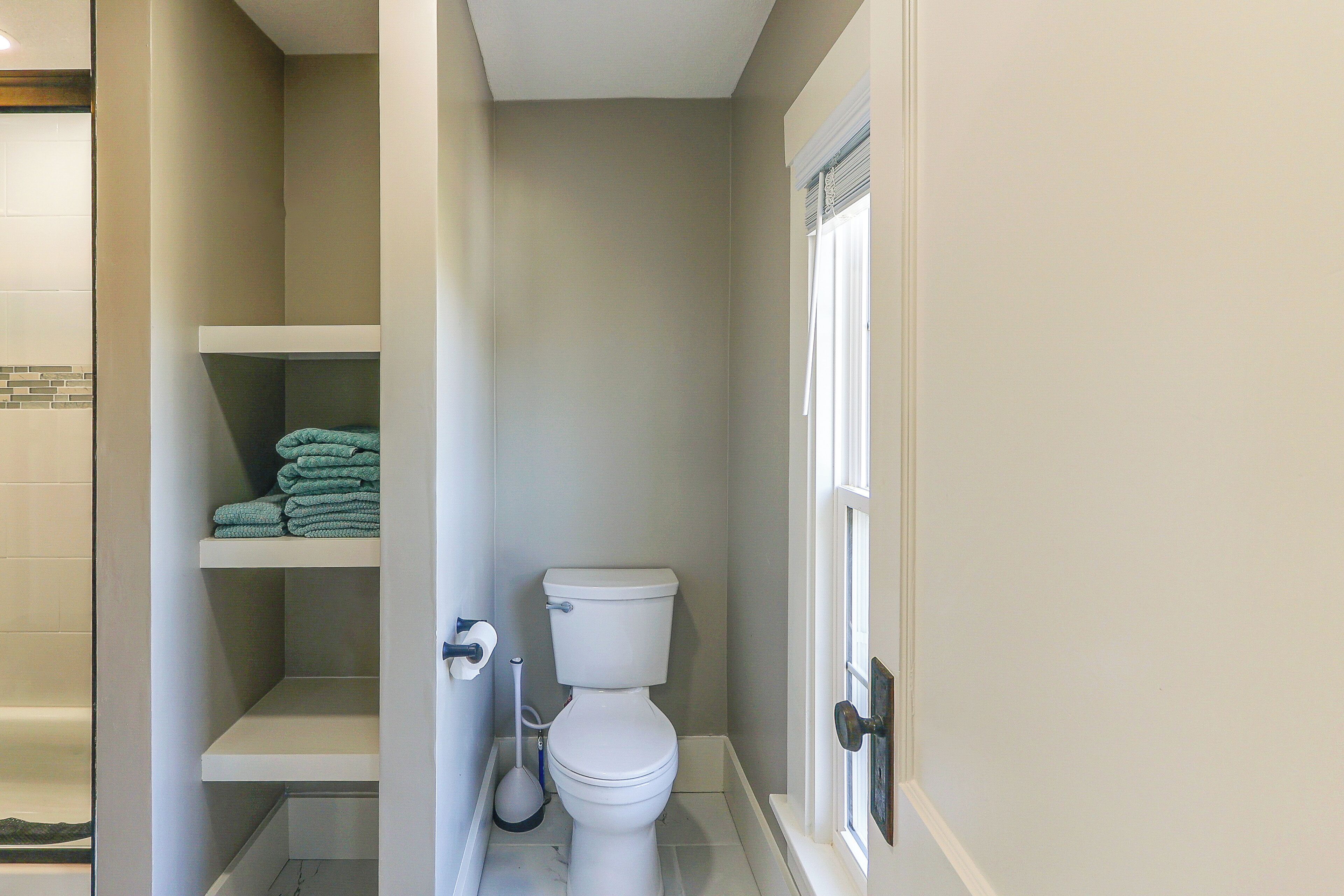 A small bathroom with a toilet, a shelf with folded towels, and a toilet brush.