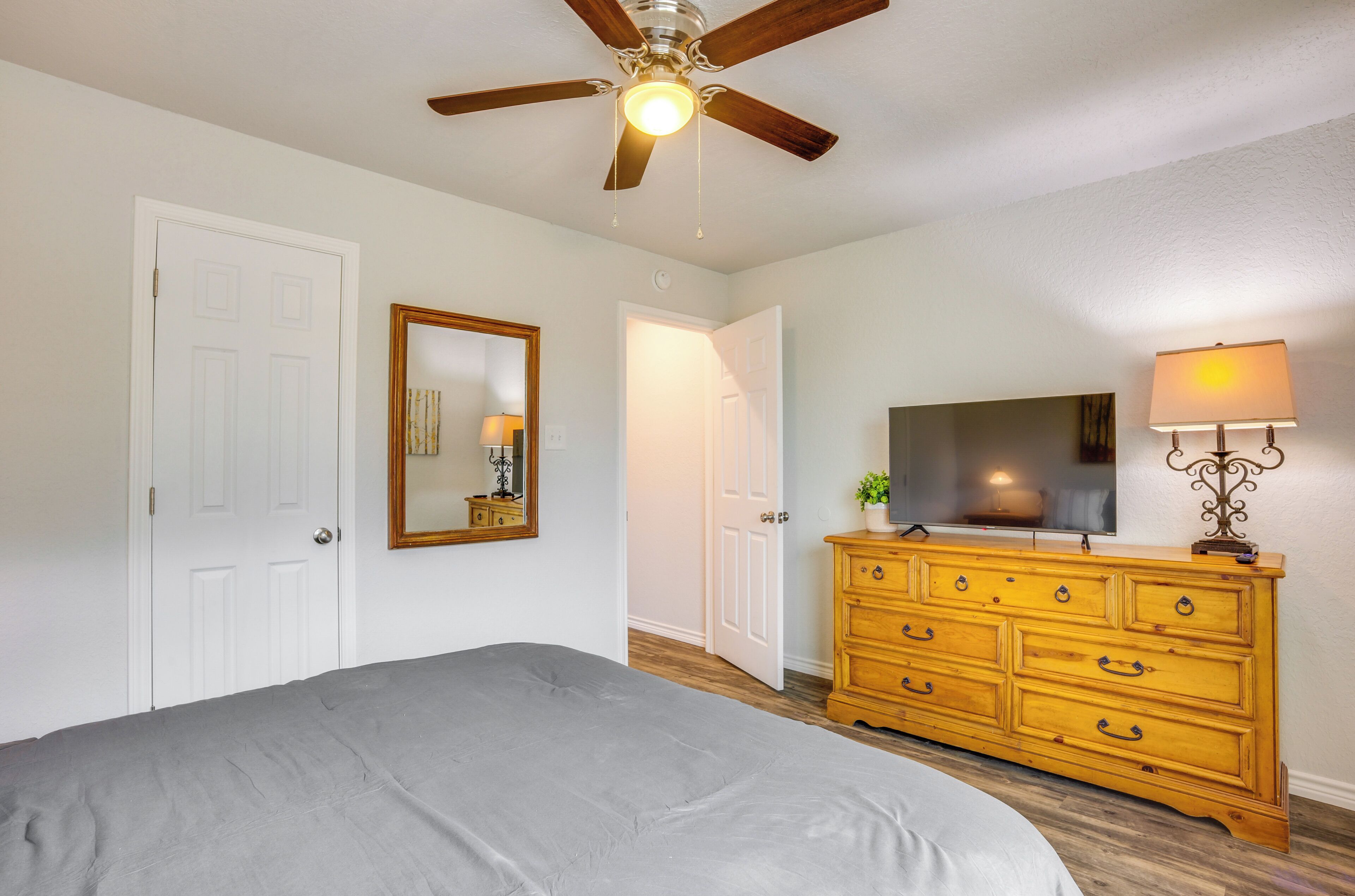 A bedroom with a bed, a wooden dresser, a ceiling fan, a mirror, and a lamp.