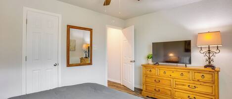 A bedroom with a bed, a wooden dresser, a ceiling fan, a mirror, and a lamp.