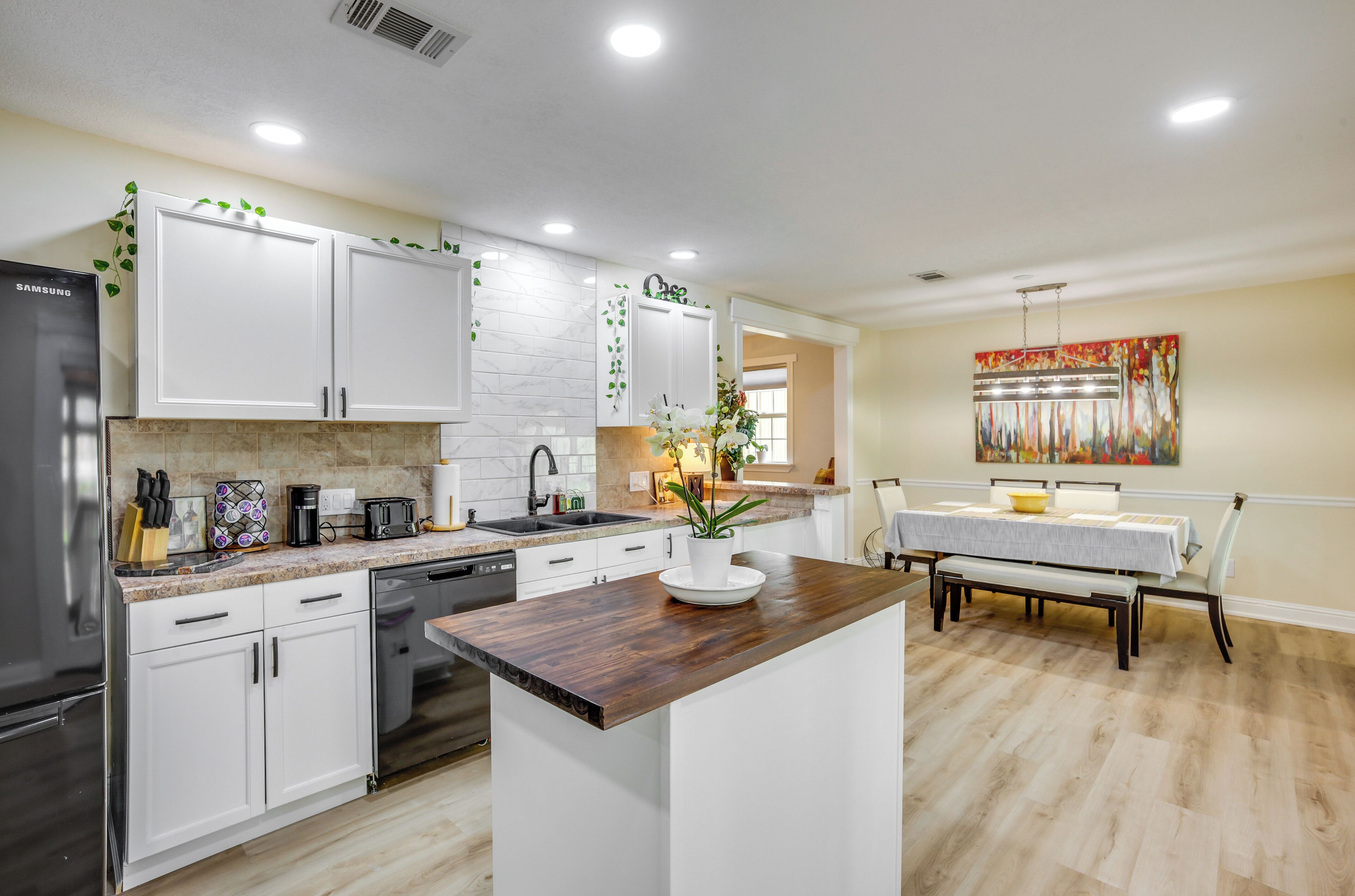 A modern kitchen with white cabinets, a central island, and a dining area with a table and chairs.