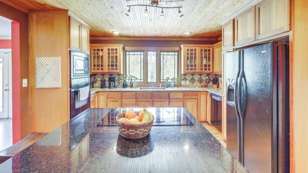 A kitchen with wooden cabinets, a granite countertop, and a stainless steel refrigerator. - Riverside Texas Retreat w/ Wraparound Porch! (Thorndale)