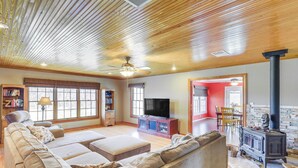 A spacious living room with a large sectional sofa, a flat-screen TV, a fireplace, and a ceiling fan. - Riverside Texas Retreat w/ Wraparound Porch! (Thorndale)