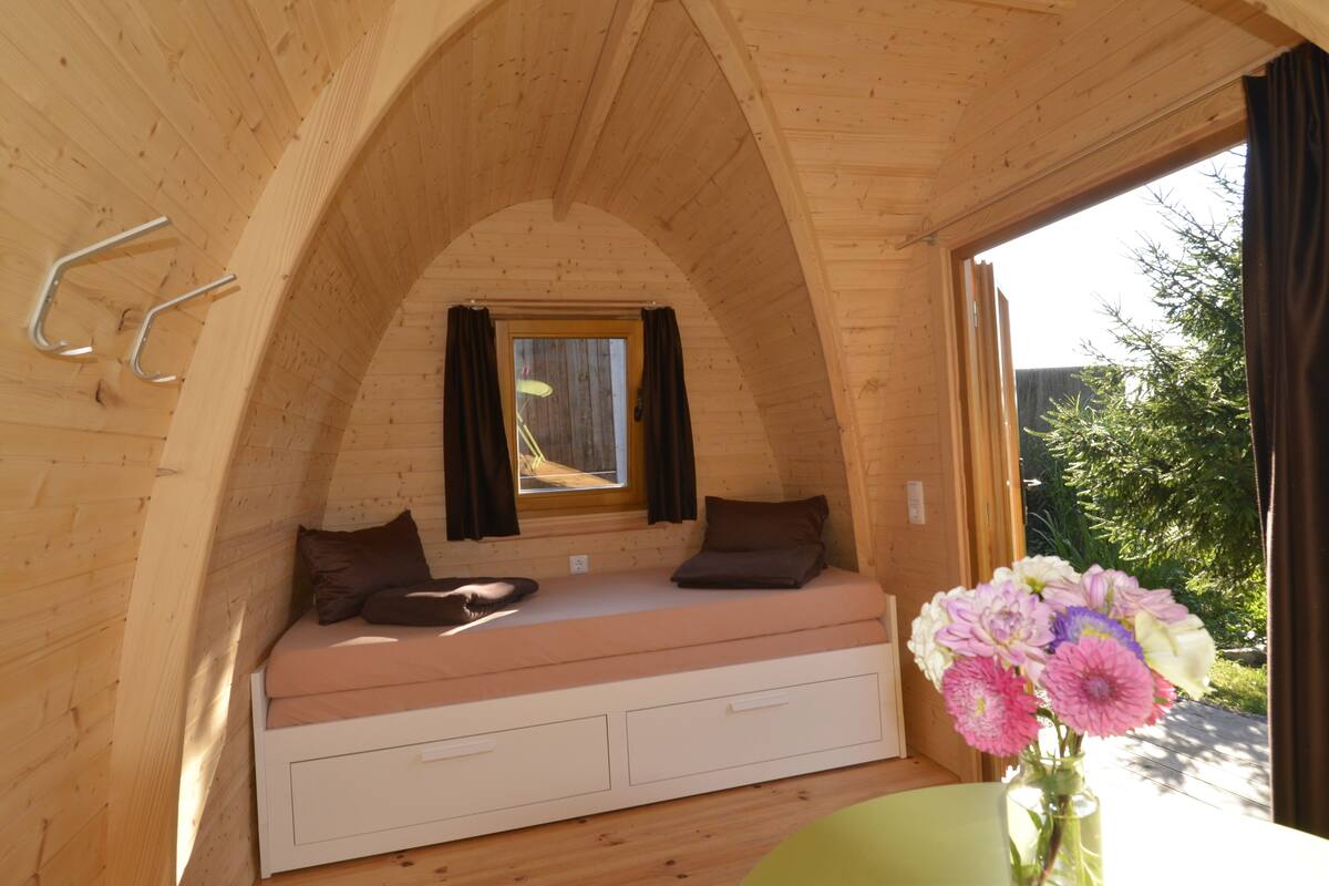 A cozy wooden cabin with a loft bed, a small window, and a vase of flowers.