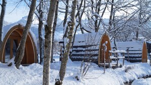 A snow-covered outdoor area with wooden structures, possibly cabins or lodges, surrounded by trees and a mountainous backdrop. - Forellensee Gstaad-Zweisimmen (Zweisimmen)