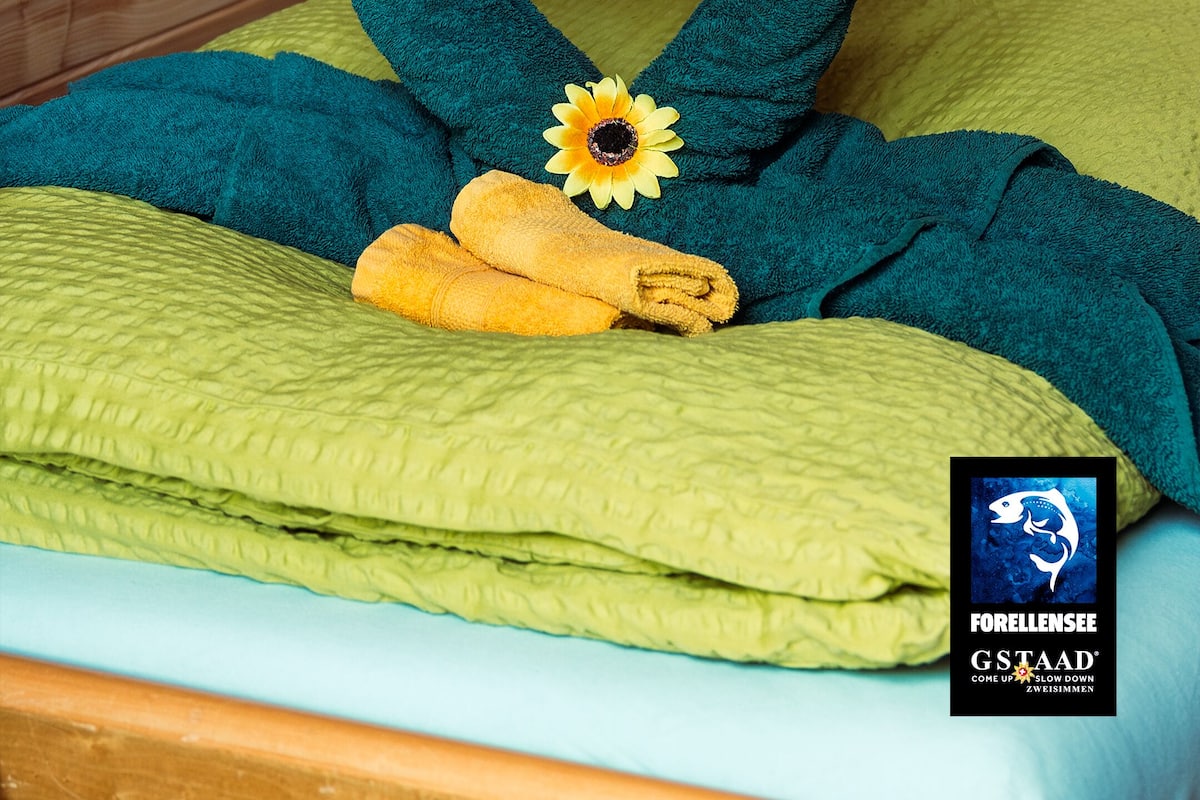 A bed with a heart-shaped towel arrangement, a yellow towel, and a sunflower decoration.