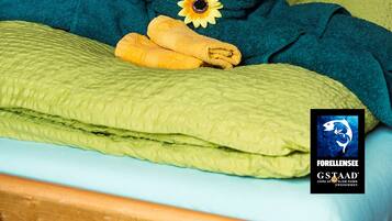 A bed with a heart-shaped towel arrangement, a yellow towel, and a sunflower decoration.