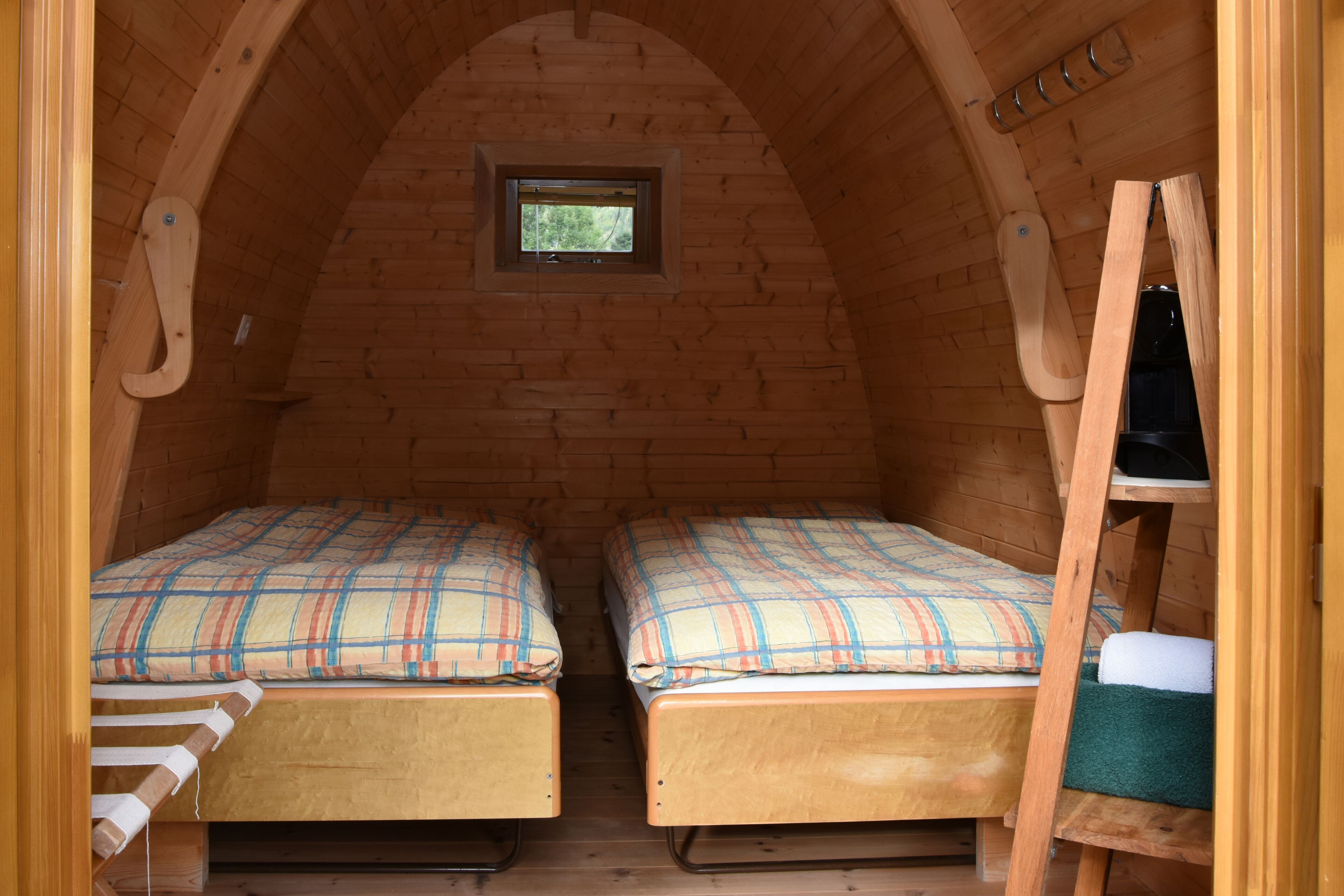 A small, cozy attic bedroom with two bunk beds, a wooden ladder, and a small window.