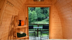 An interior view of a wooden cabin with a loft bed, a small table with chairs, and a view of a forested area outside. - Forellensee Gstaad-Zweisimmen (Zweisimmen)