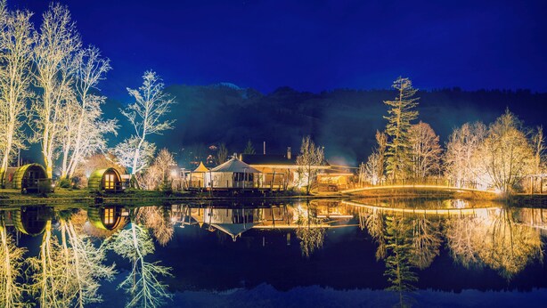 A lakeside property with a reflection of the buildings and trees, a covered bridge, and a mountain backdrop. - Forellensee Gstaad-Zweisimmen (Zweisimmen)