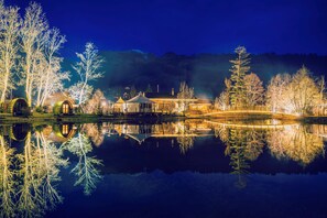 A lakeside property with a reflection of the buildings and trees, a covered bridge, and a mountain backdrop. - Forellensee Gstaad-Zweisimmen (Zweisimmen)