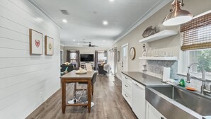 A modern kitchen with a wooden dining table, white cabinetry, and a stainless steel sink. - Pinewood Cottage 2 Bedroom Home by RedAwning (Panama City Beach)