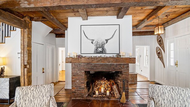 Una habitación amplia con chimenea de ladrillo, sillones estampados y una obra enmarcada sobre la repisa.