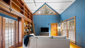 Una sala de estar con sofá, estanterías de madera, televisor y un amplio ventanal con vistas a árboles.