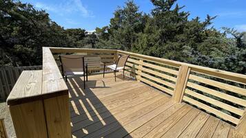 Enjoy outdoor dining or relaxation on this deck with benches and tables, surrounded by a railing and lush trees.