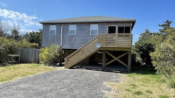 Une maison à deux étages dotée d’une terrasse en bois et d’un escalier menant à la porte d’entrée.