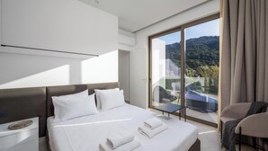 A modern hotel room with a large bed, a nightstand, a chair, and a balcony with a view of the hills. - Casa Yiava with private pool (Ialysos, Dodecanese)