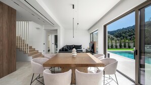 A modern dining area with a wooden table and chairs, a kitchen in the background, and a pool view. - Casa Yiava with private pool (Ialysos, Dodecanese)
