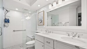 Un bagno moderno con cabina doccia in vetro, un water e un mobile lavabo con due lavandini.