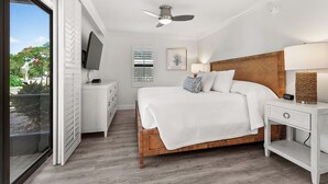 Una camera da letto con un letto, un comodino, una TV, una ventola a soffitto, una finestra con tende e vista sull'esterno.