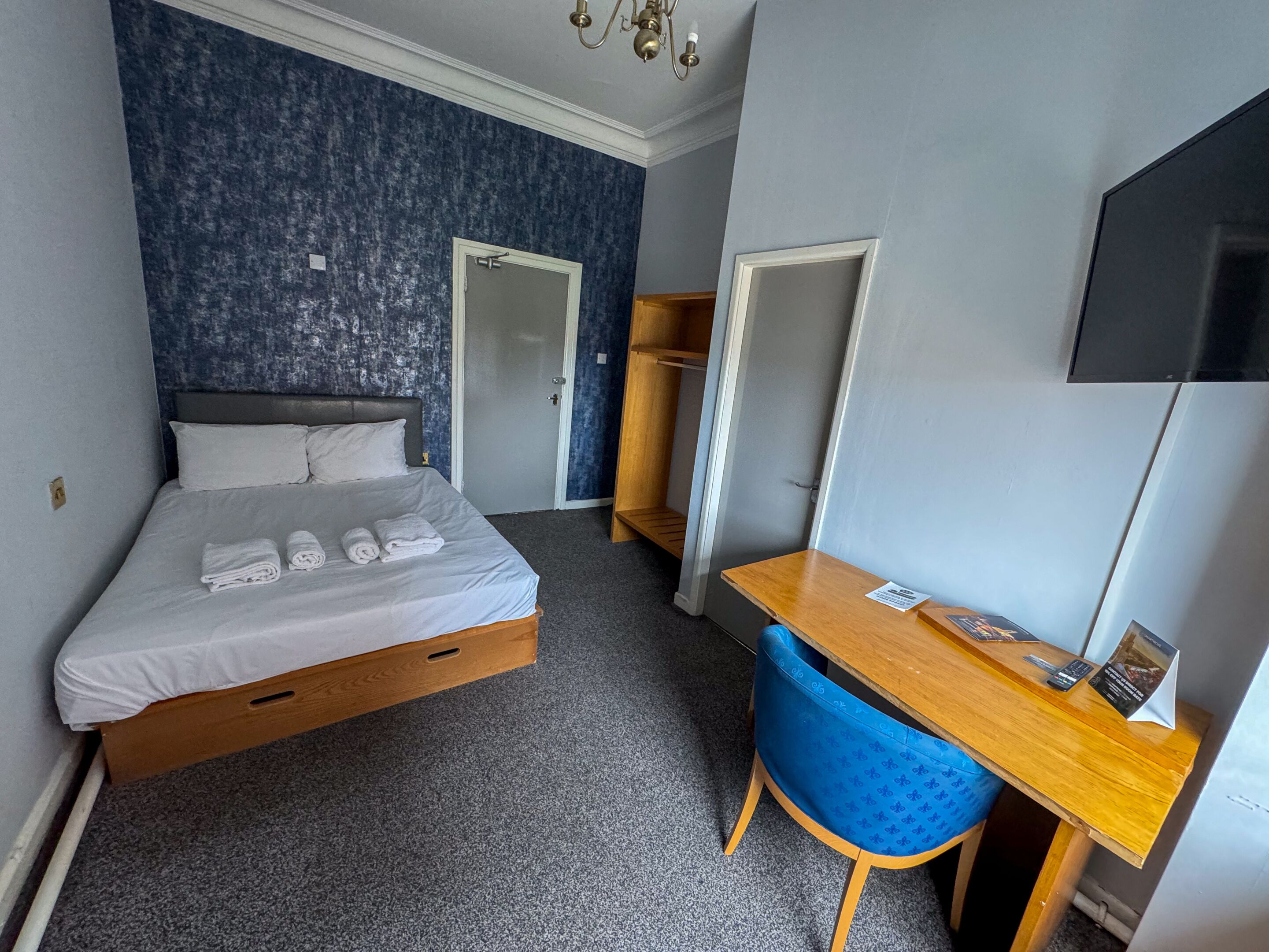 A hotel room with a bed, a desk, a chair, a TV, and a wardrobe.