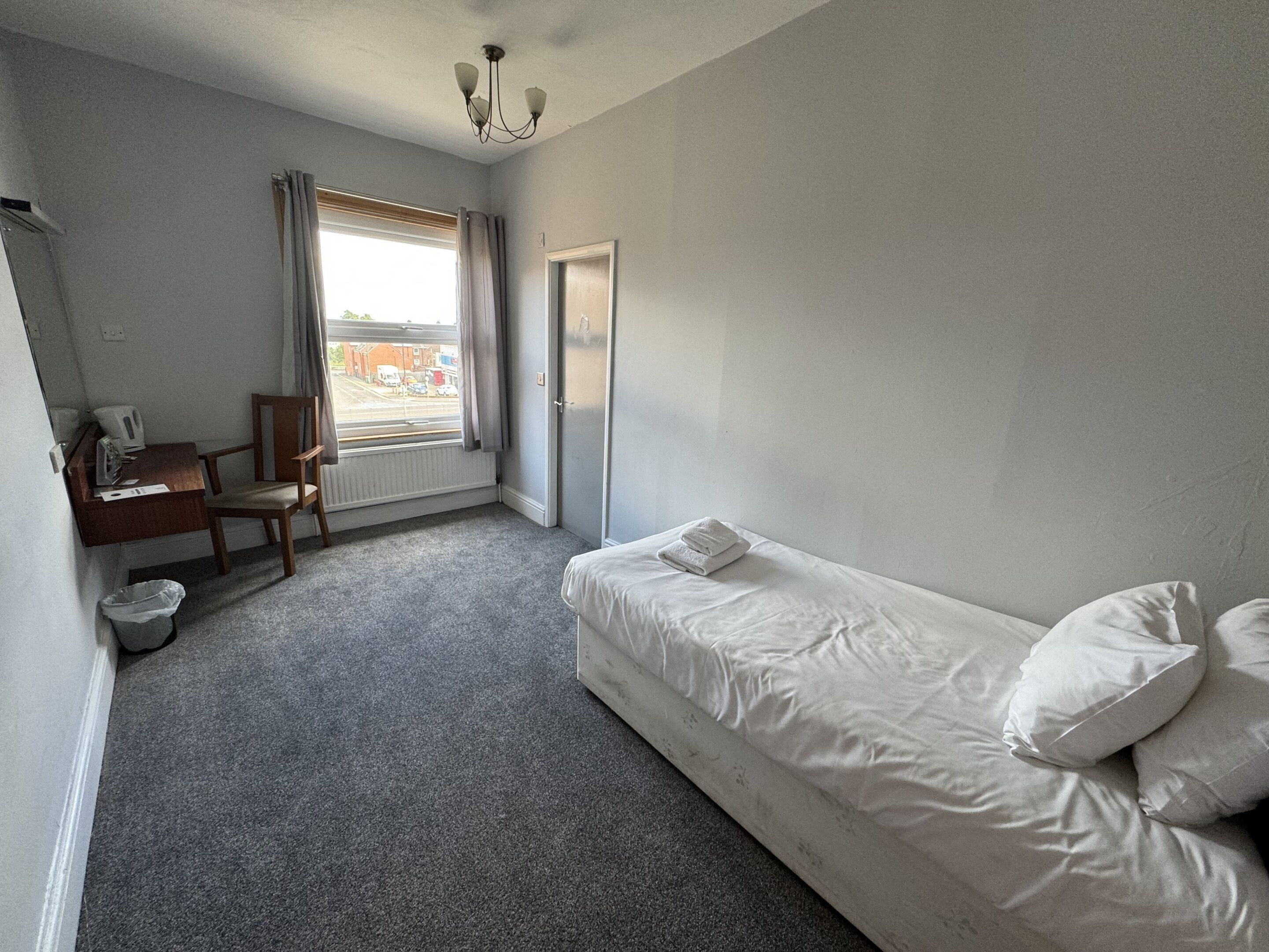 A small, sparsely furnished room with a single bed, a desk, and a chair.