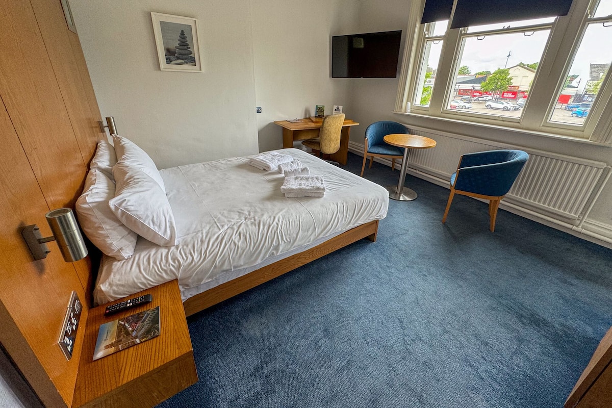 A hotel room with a bed, a desk, a chair, a TV, and a window with a view of the outside.