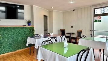 A hotel room with a green wall, white curtains, and a flat-screen TV mounted on the wall.