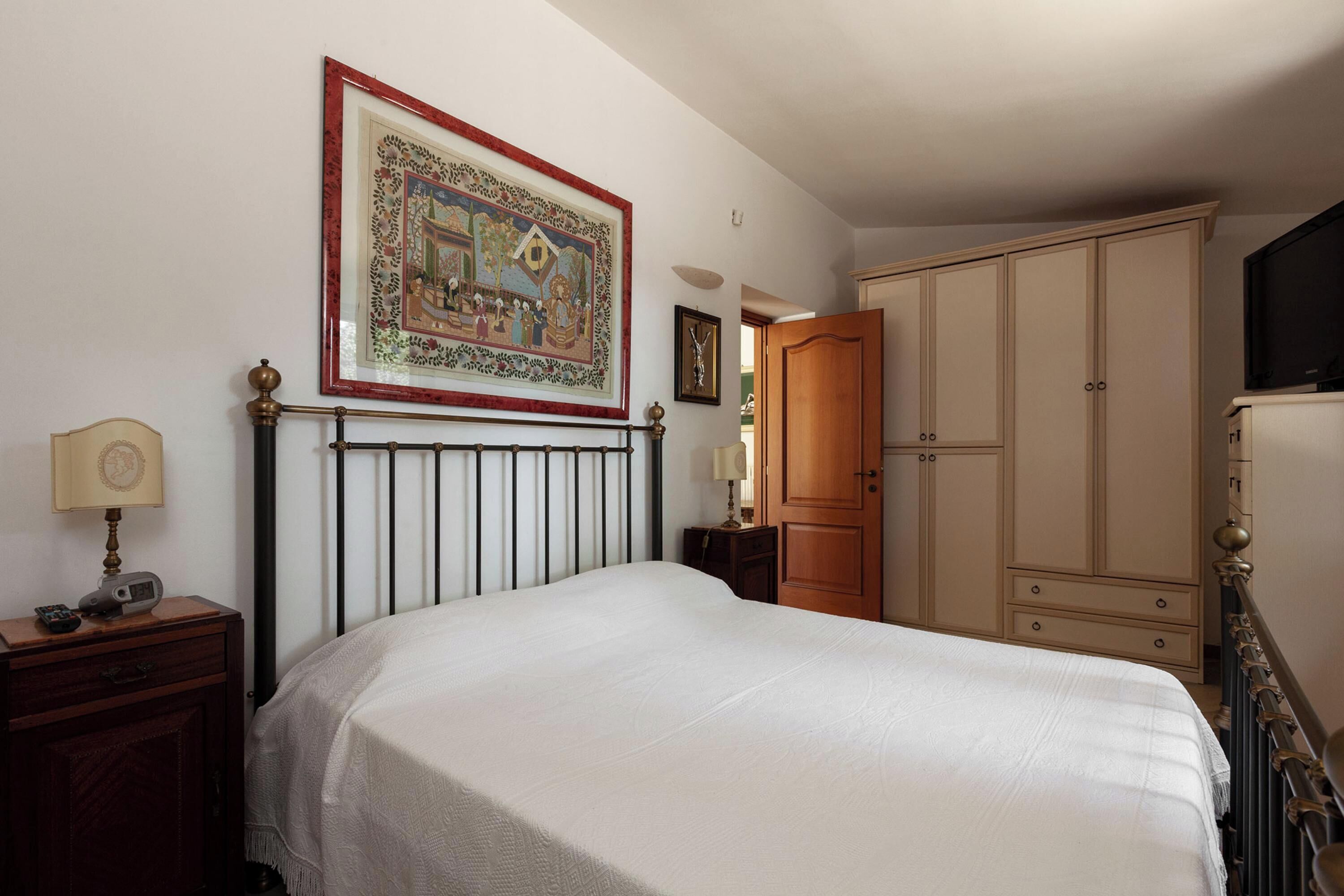 Un dormitorio con cama, armario, televisor y un cuadro en la pared.