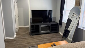 A bedroom with a TV on a stand, a bed with a quilt, a wooden nightstand, and a mirror.