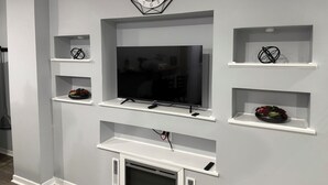 A modern living room with a large flat-screen TV mounted on a white wall, surrounded by white shelving units.
