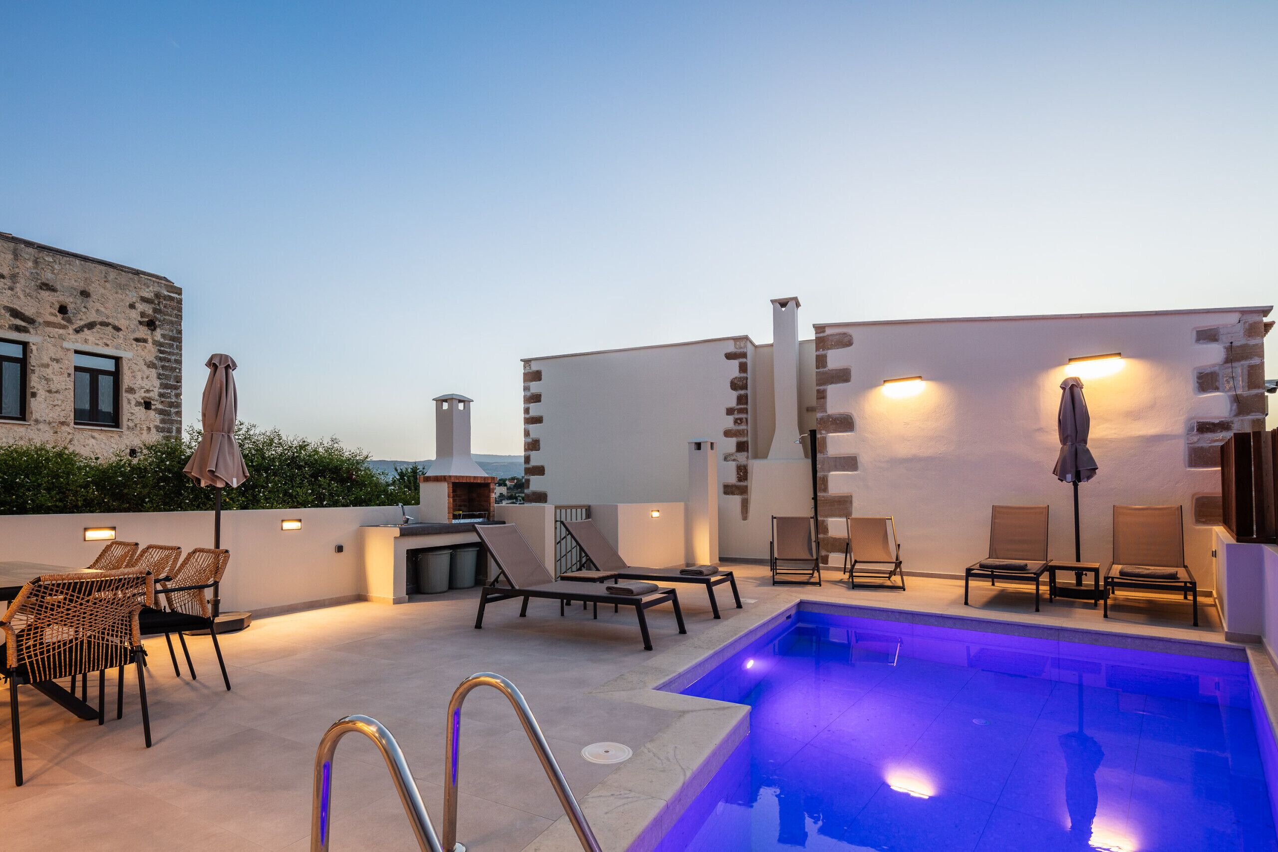 An outdoor pool area with lounge chairs and umbrellas, a poolside bar, and a view of the cityscape.